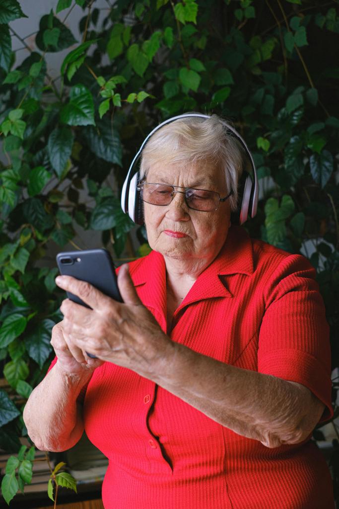an elderly lady with headphone over her ears and looking at a mobile phone